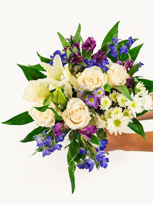 A vibrant bouquet featuring cream roses, purple blooms, and lush greens, ideal for gifts.