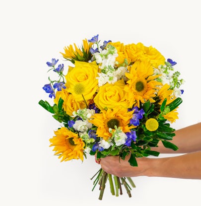 Vibrant bouquet of yellow roses, sunflowers, and blue delphiniums, perfect for celebrations.