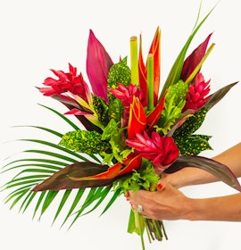 Vibrant tropical bouquet featuring pink ginger flowers, lush green leaves, and dramatic red accents.