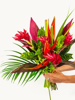 Vibrant tropical bouquet featuring pink ginger flowers, lush green leaves, and dramatic red accents.