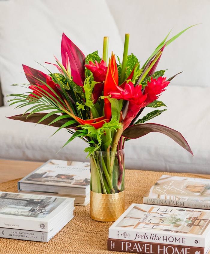 Vibrant tropical floral arrangement featuring red blooms and lush green leaves in a vase.