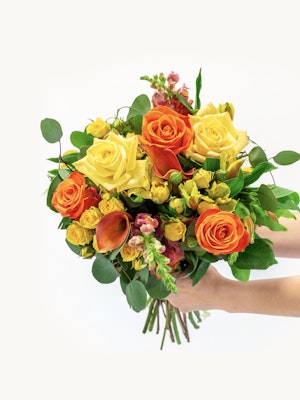 Vibrant bouquet of yellow and orange roses with lush greenery, perfect for any celebration.