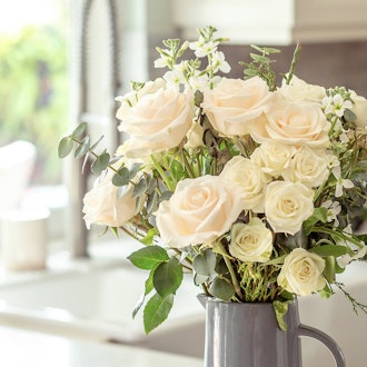 Elegant arrangement of white and soft pink roses with greenery in a charming vase.