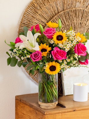 Vibrant floral arrangement featuring pink roses, sunflowers, and white lilies in a glass vase.