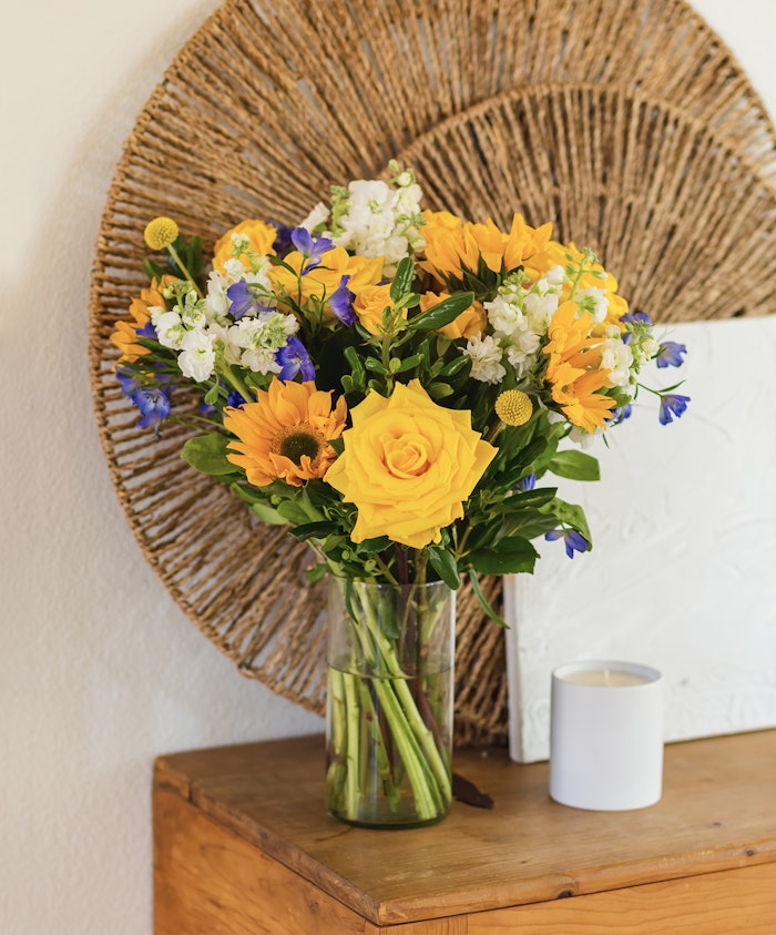 Vibrant bouquet of yellow roses, sunflowers, and seasonal blooms in a glass vase.