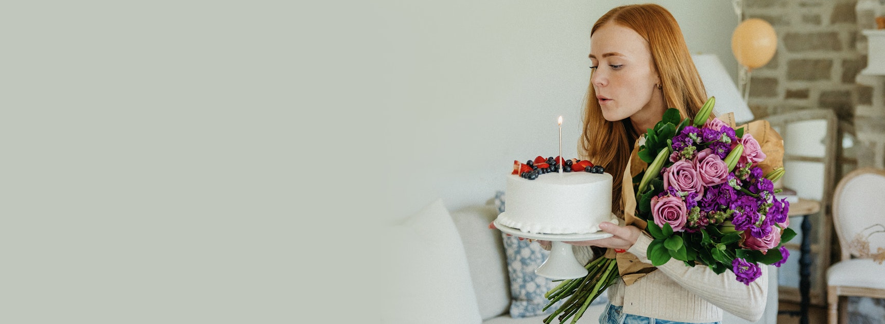 A woman holds a beautiful bouquet and a birthday cake, celebrating a special occasion with joy.