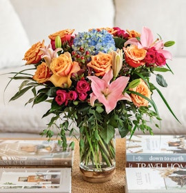 Vibrant floral arrangement featuring roses, hydrangeas, and lilies in a chic glass vase.
