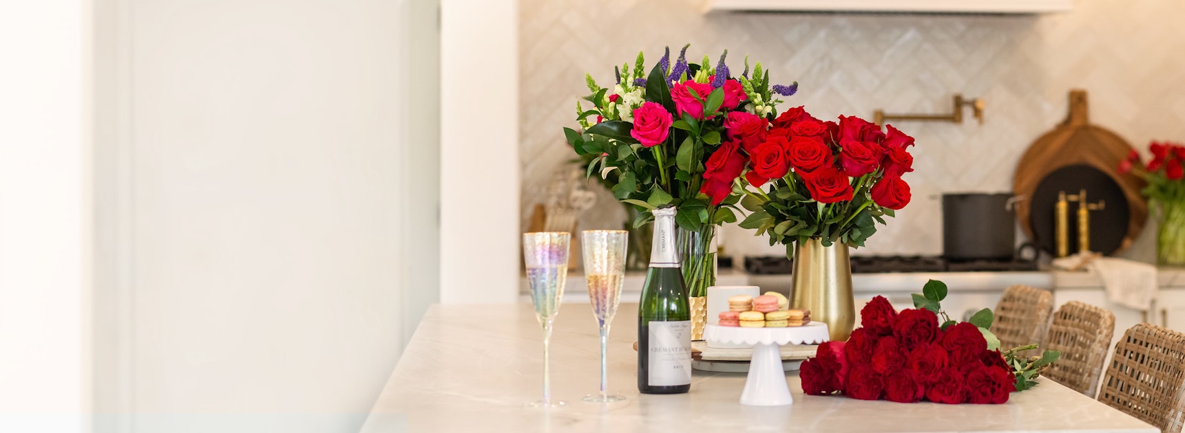 Elegant floral centerpiece with red roses and purple accents, paired with champagne and macarons.