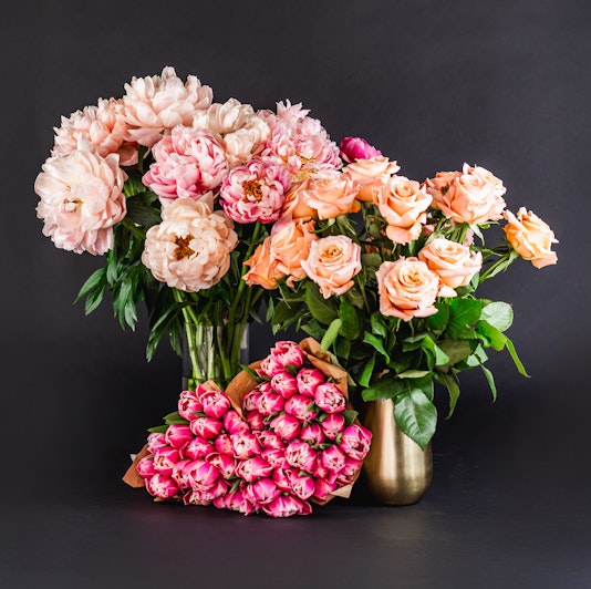 A vibrant arrangement of peonies and peach roses in elegant vases against a dark background.