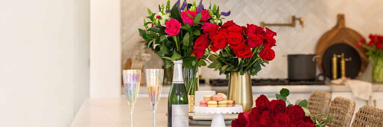 Vibrant floral arrangements with red roses and colorful treats set on a kitchen counter.